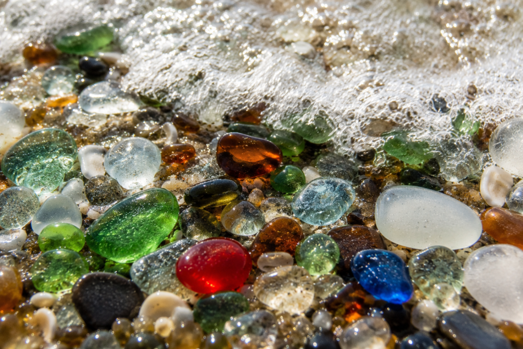 Close-up of smooth, multicolored sea glass pebbles on wet sand at Glass Beach